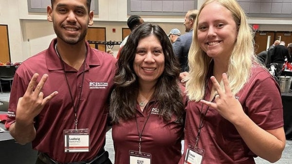 Two ASU business students and an ASU faculty member smile and make a pitchfork symbol with their hands.