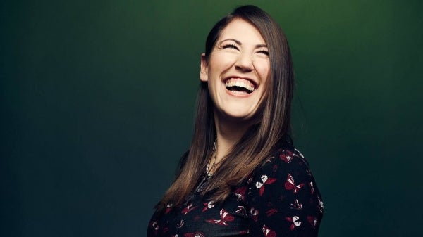 A woman looks up and to the right while smiling broadly against a solid green background