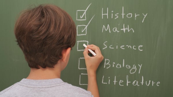 Person writing school subjects on a blackboard