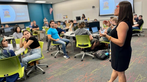 Woman standing at the front of a classroom speaking to students.