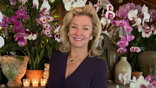 Woman smiling in front of a backdrop of flowers.