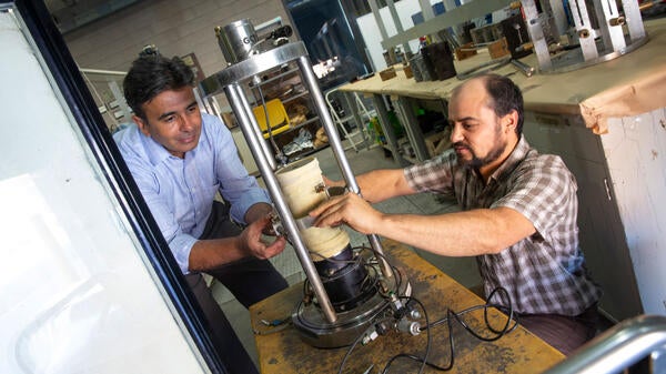 Two people load a pavement sample into a piece of testing equipment.