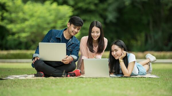 students work on laptops while sitting on a lawn