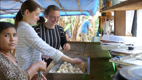 Three people stand looking into a tray of items.