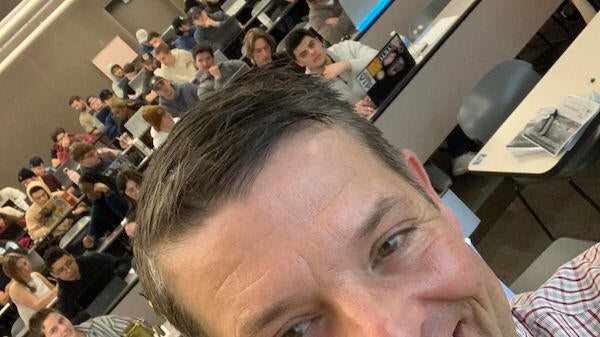 Timothy Becker taking a selfie with students sitting in a lecture hall.