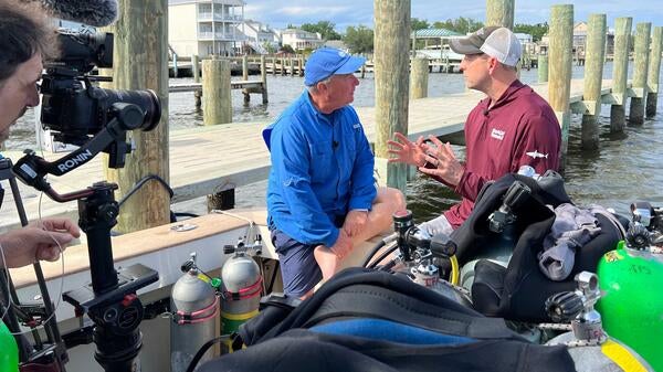 Two people talking on boat being filmed for TV show