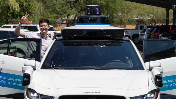 Two people stand next to the open doors of a white car.