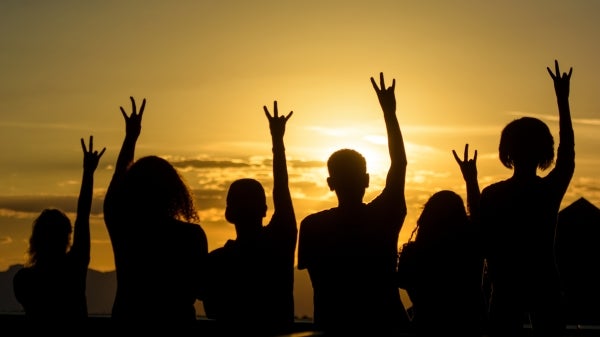 A group of students silhouetted by the setting sun hold up pitchfork gestures