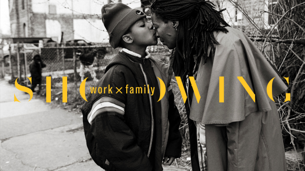 African American boy kisses mother's nose as she bends down to him, both standing on a city block