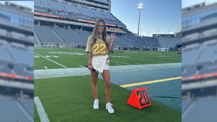 ASU grad Courtney Robinson makes the ASU pitchfork sign on a football field.