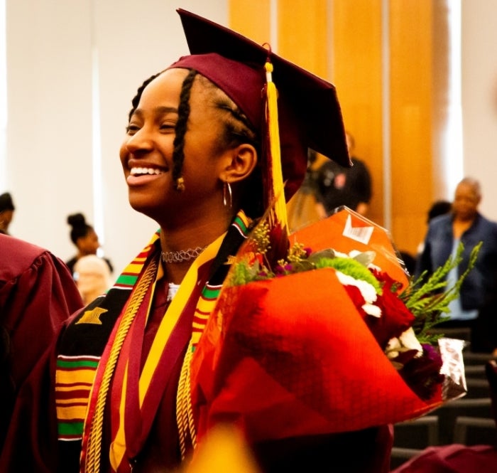 Student wearing a cap and gown and holding flowers.