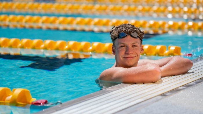 Portrait of college male resting in pool with elbows propped up on deck