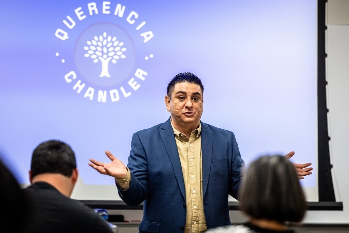 Man speaking in front of projection screen to audience