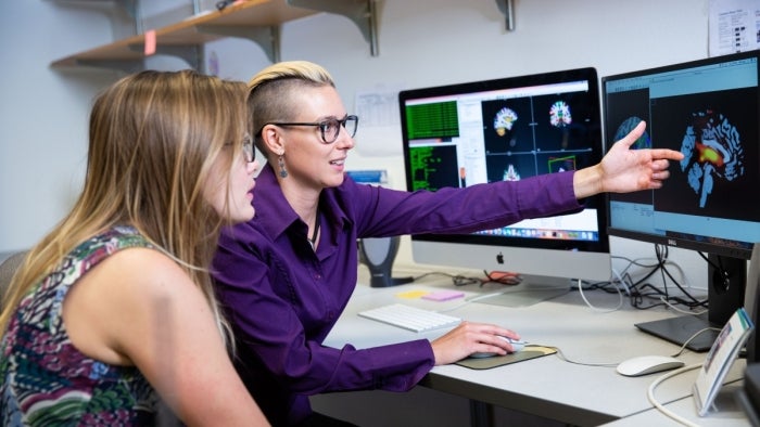 Two people looking at a computer screen as one gestures and speaks.