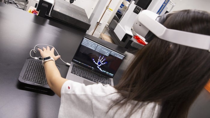 A student holds hand over a touch pad while wearing a VR headset.