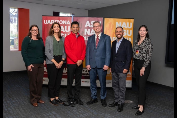 Group of faculty and business leaders pose in front of signs for ASU, NAU and UfofA.