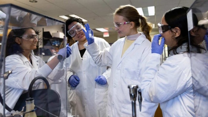 Lab students gathered in a lab wearing lab coats.