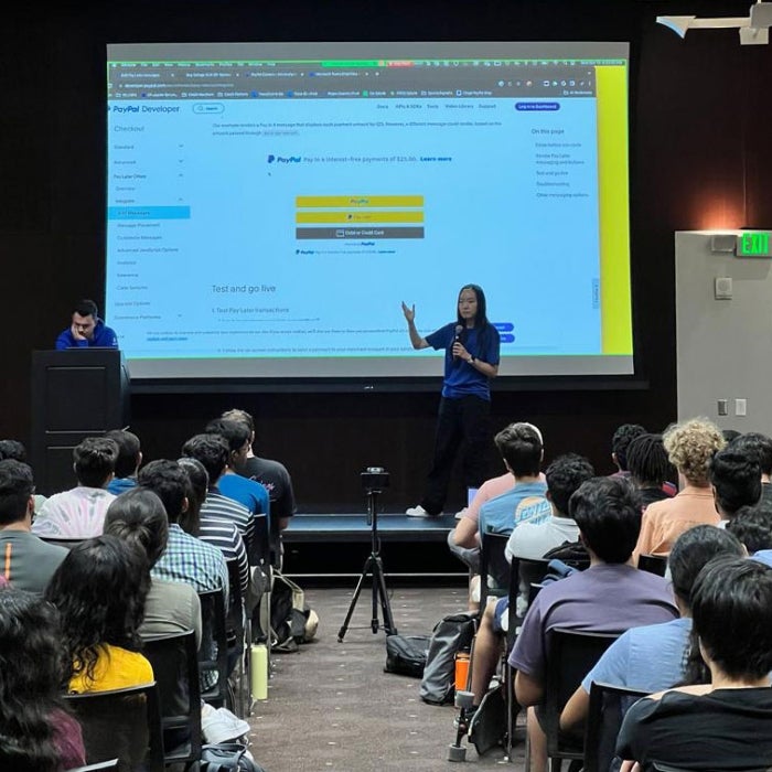 Woman giving a presentation to a large audience as she points to a screen.