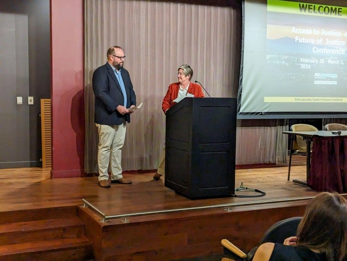 Man and woman standing onstage in front of an unseen audience.