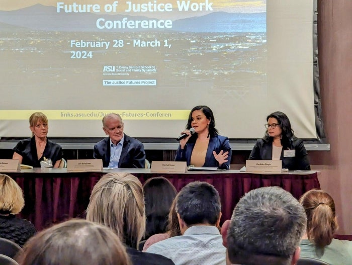 People seated at a panel table speaking to an audience.