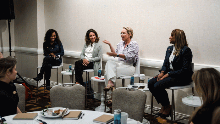 Four women speak on a panel in front of a lunch audience