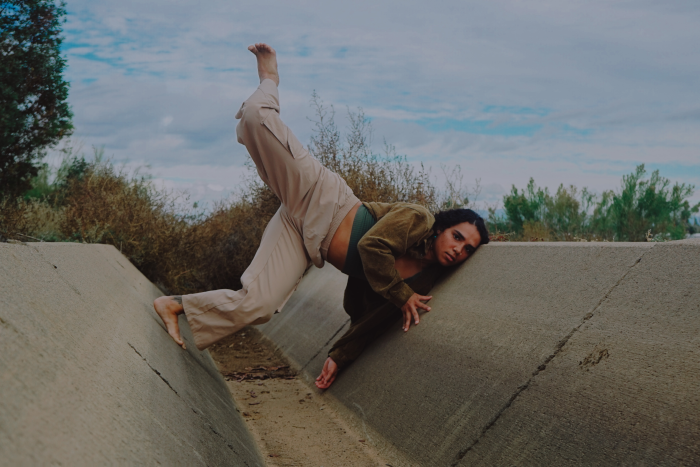 A dancer poses with leg extended against a concrete wall