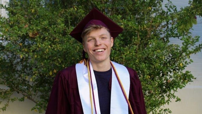 ASU grad Tristan Tierce smiles in his graduation cap and gown