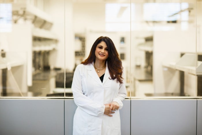 Bimonte-Nelson wears a lab coat and stands in front of a window looking into a lab space