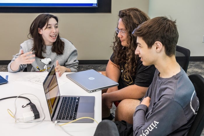 3 high school students talk at a table