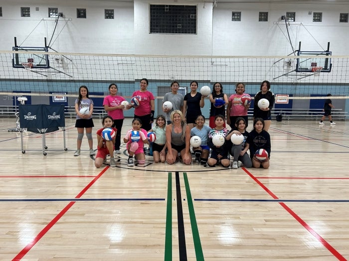 Girls pose holding volleyballs in a gym