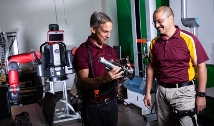 Two men look at a robot.