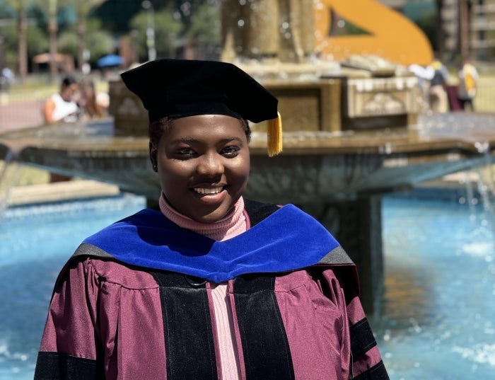 A smiling woman in graduation robes in front of a fountain.