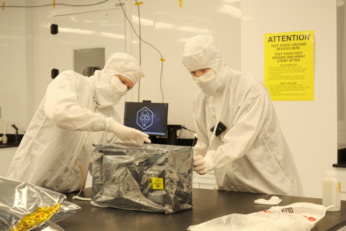 Two people wearing lab gear inspect an item