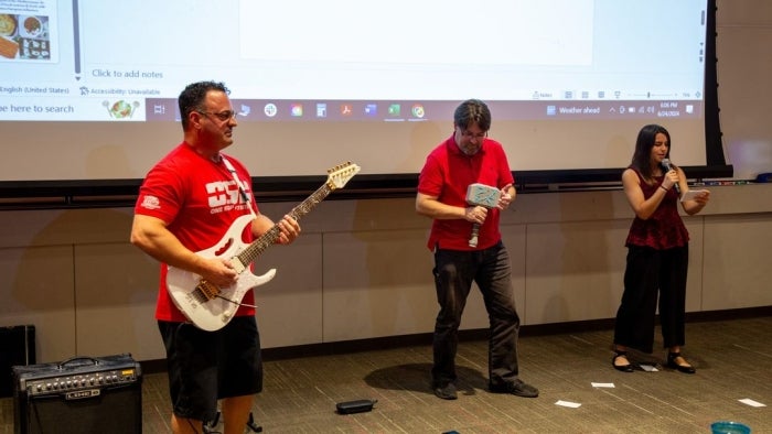 Two men play guitar while a woman sings.