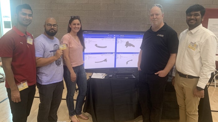 Five people pose in front of a monitor displaying the bone atlas application