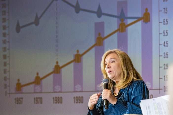 Woman speaking into microphone with bar graph on a presentation screen behind her