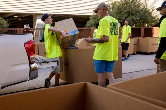 Volunteers wearing bright yellow shirts unload items into boxes from the back of a truck