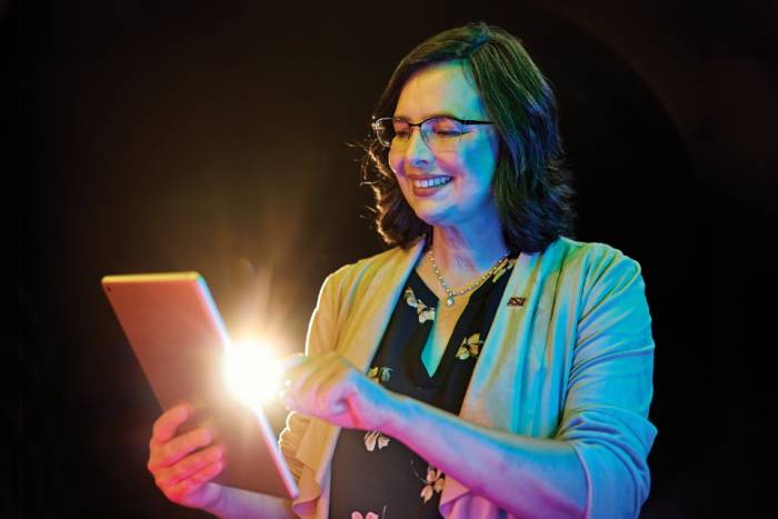 Woman with dark hair and glasses in a light blazer interacts with an tablet