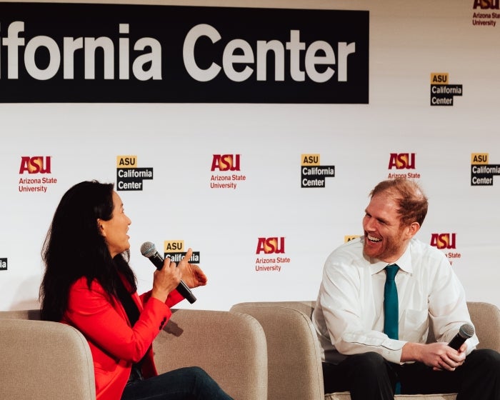 Woman speaking into microphone while man sits next to her listening