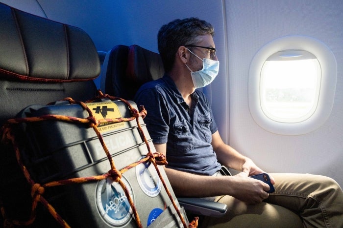 A man sits on a plan with a suitcase on the seat next to him