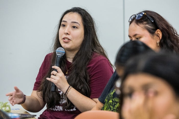 Student in a maroon t-shirt speaking into a microphone