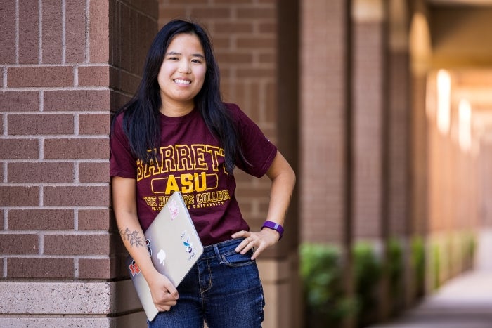 Portrait of a young woman leaning against a pillar holding a laptop