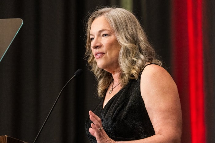 Blonde woman in black dress speaks into microphone