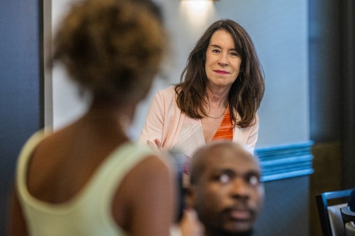 A white woman with long dark hair looks at a person asking a question, whose back is turned to the camera 