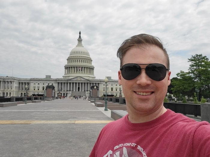 A man with sunglasses stands in front of the U.S. Capitol building on an overcast day.