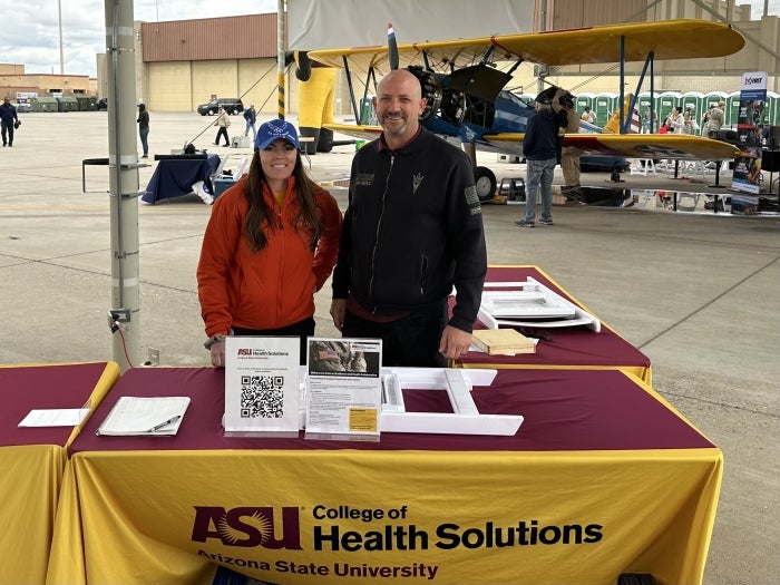 Man and woman standing behind a booth at a tabling event.