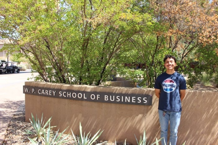 Student Joseph Espinoza stands smiling outside in front of the W. P. Carey business school sign