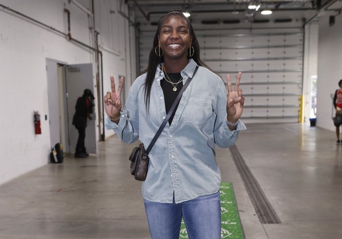 A woman smiles while making two peace signs with her hands