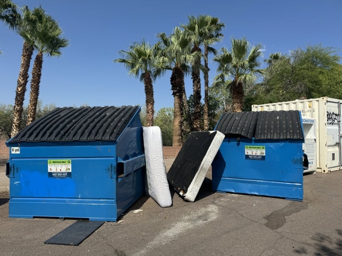 Discarded mattresses leaning against two City of Tempe dumpster boxes