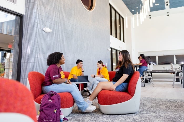 Students hang out in oversized red chairs in the lounge area of a residential hall